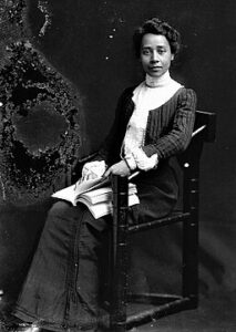Dr. Anna Julia Cooper sitting in chair with book on her lap.